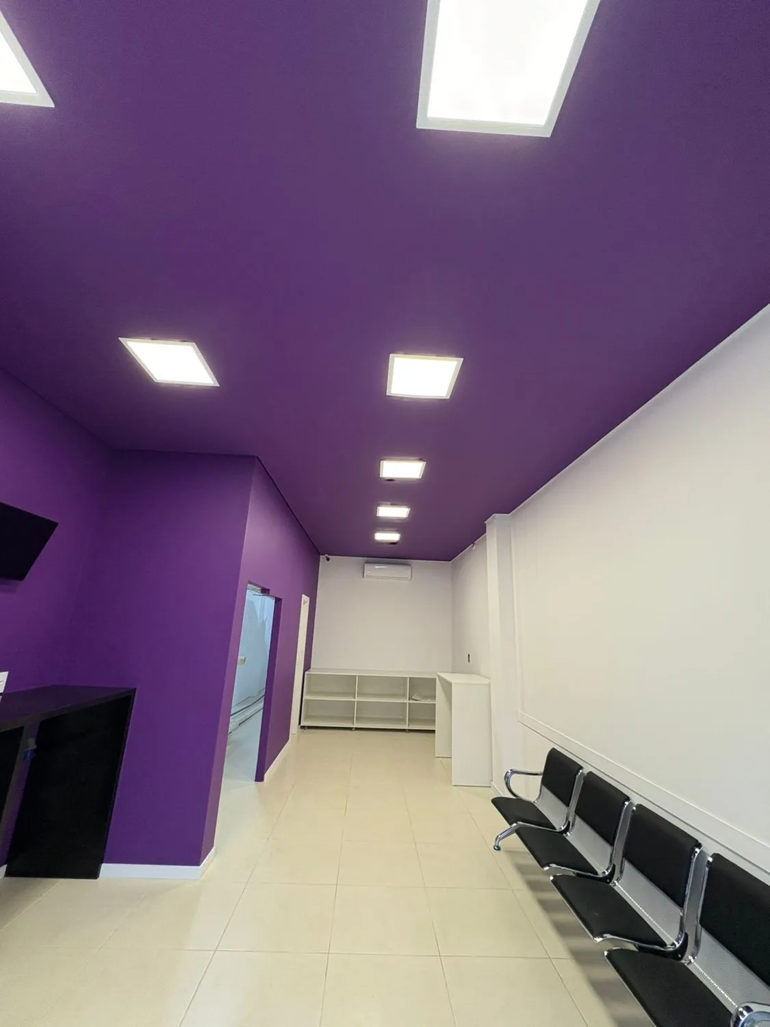 Franquia Lavô: recepção com parede roxa, forro com iluminação embutida e porcelanato claro
