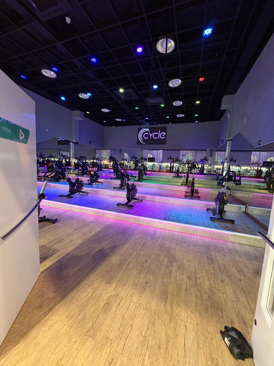 Reforma Ultra Academia: estúdio de bike com piso de madeira e iluminação cênica